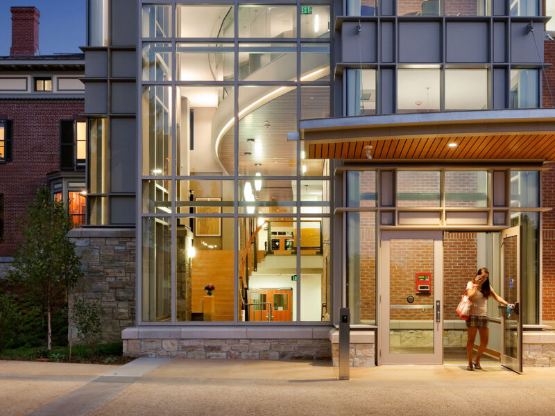 student on the phone exiting Champlain College's Perry Hall Welcome Center at night