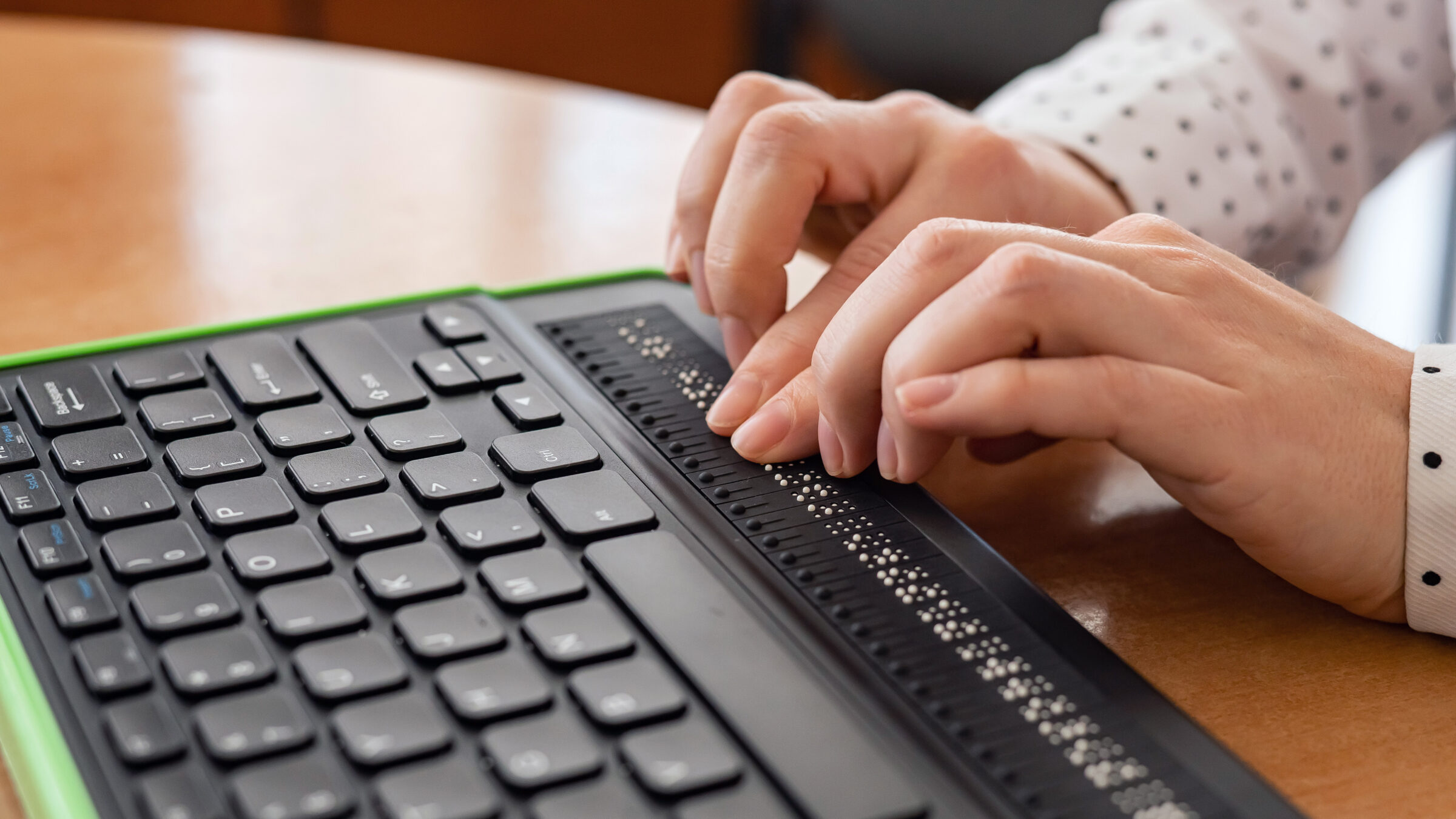 A blind woman uses a computer with a Braille display and a computer keyboard. Inclusive device