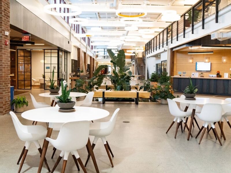 a two-floor building with various working spaces, including small and large wooden tables, benches, and plants
