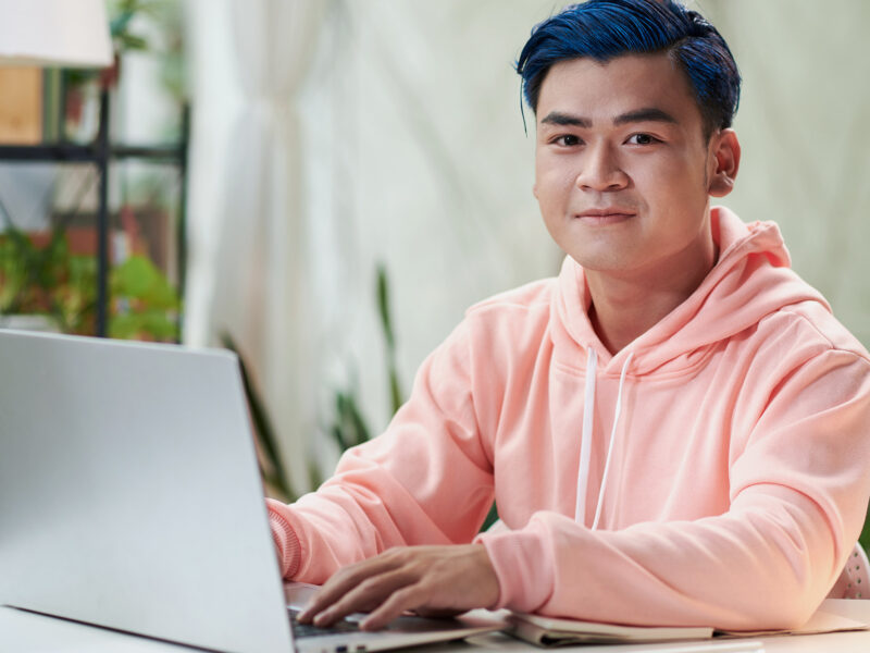 young man with blue hair is using a laptop