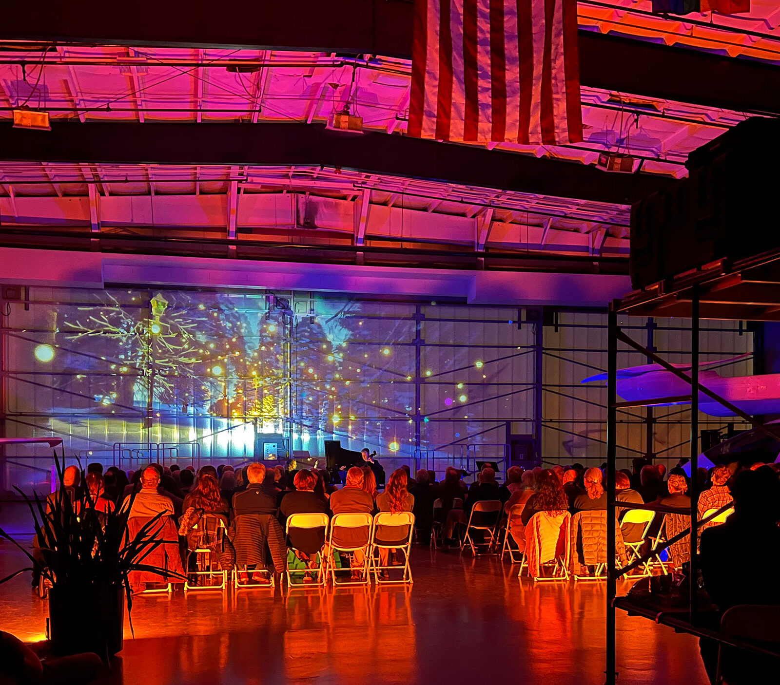 Projection art on display inside an airplane hangar, accompanied by an orchestra.
